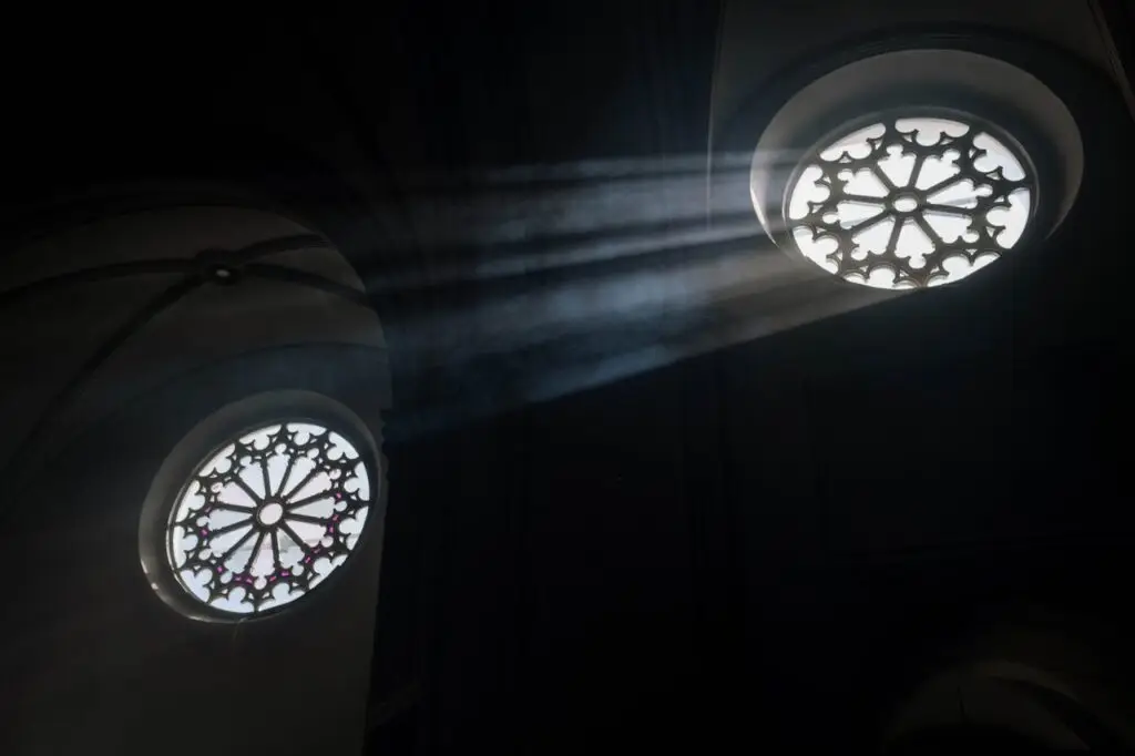 Sun rays illuminate ornate church rose windows, creating a dramatic interior scene.